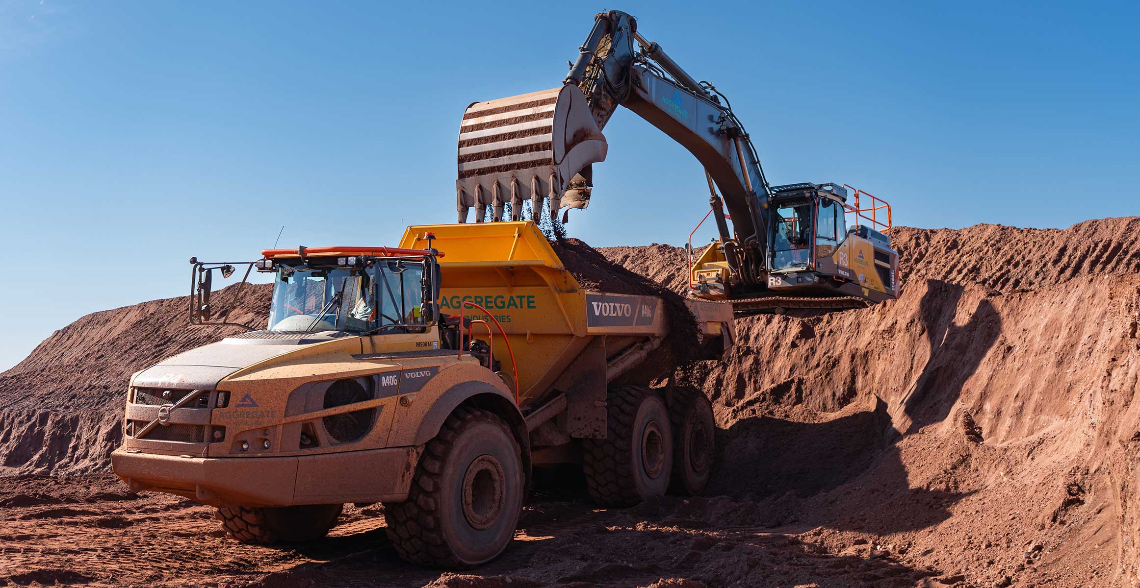 Excavatrice Volvo chargeant un camion benne sur un chantier de terrassement sous ciel bleu